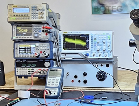 Pohled na stůl: osciloskop, multimetr, pájka, měřák kondenzátorů.